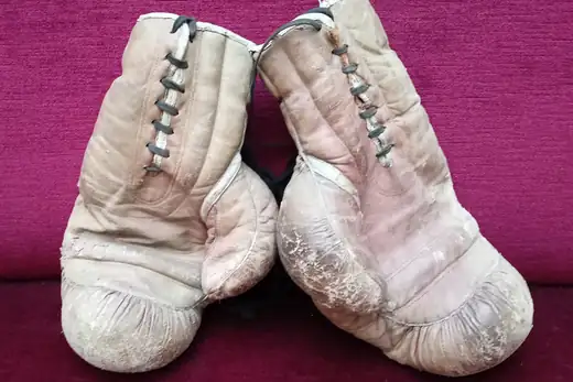 Abgenutzte helle Boxhandschuhe auf rotem Stoff