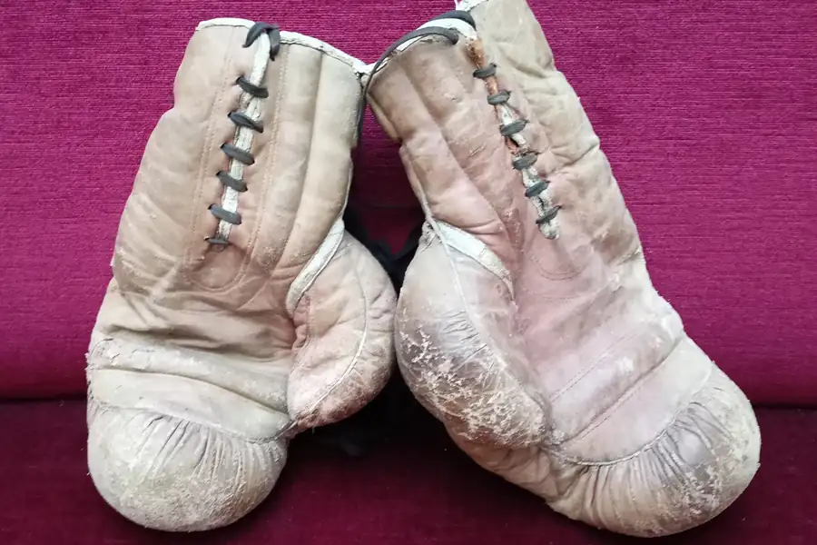 Abgenutzte helle Boxhandschuhe auf rotem Stoff