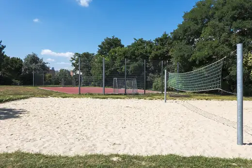 Grosses Sandfeld mit gr&uuml;nem Netz, dahinter ein Hartplatz hinter einem Zaun