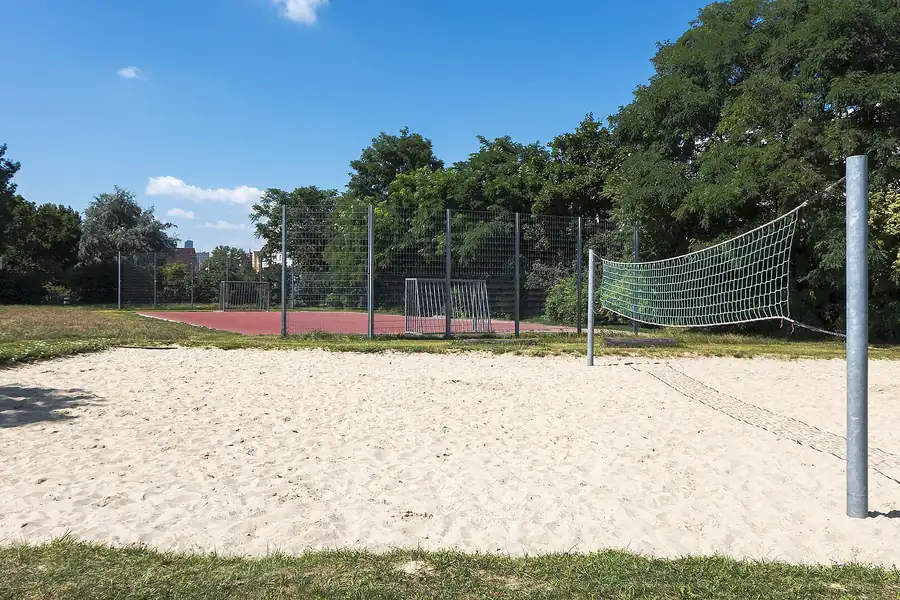 Grosses Sandfeld mit grünem Netz, dahinter ein Hartplatz hinter einem Zaun