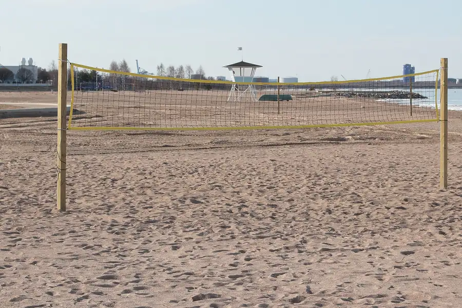 Volleyballnetz mit gelber Randleine auf einem weiten Sandplatz am Ufer